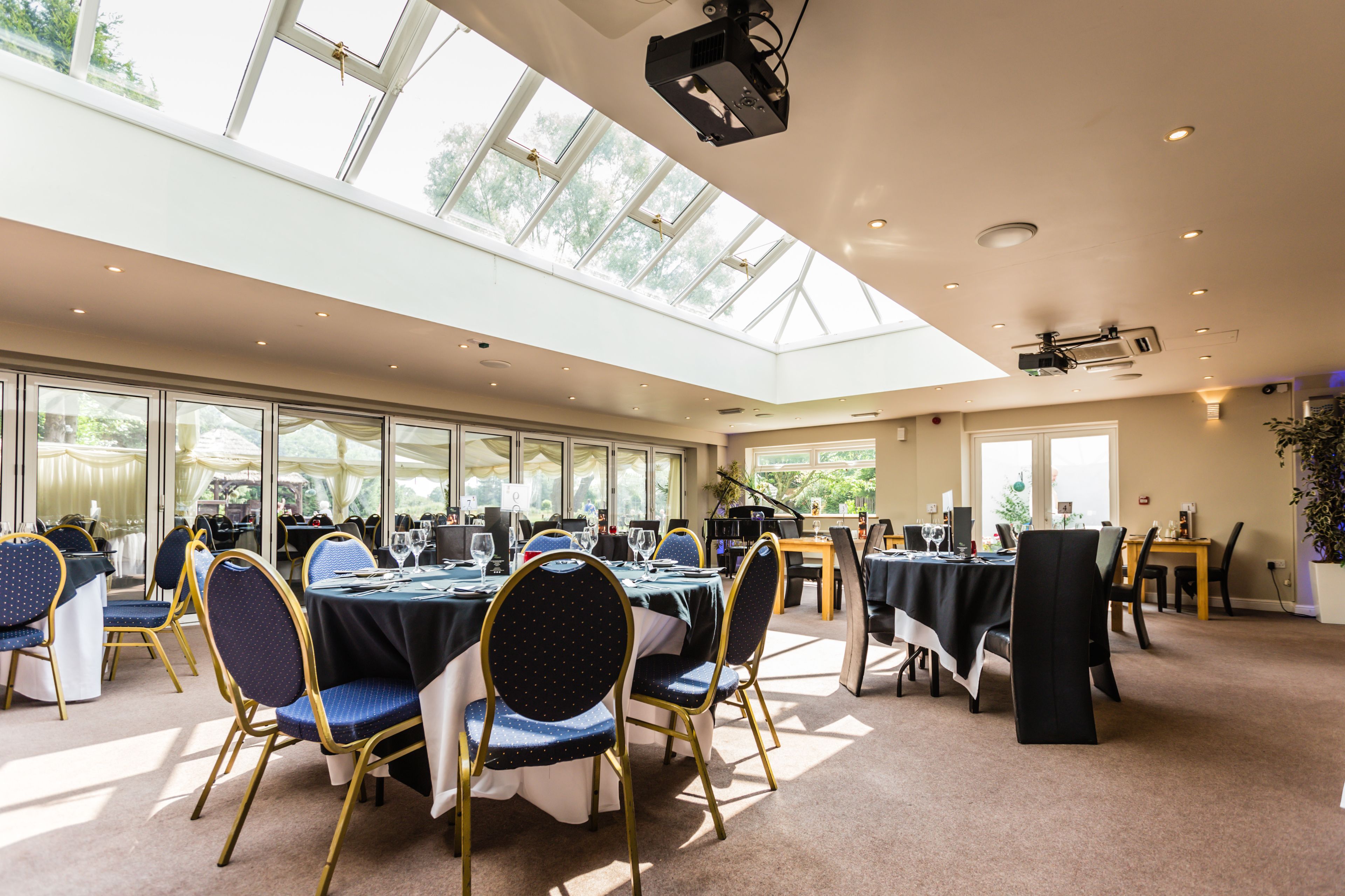 A spacious conference room with multiple tables and chairs, large windows, and a skylight.
