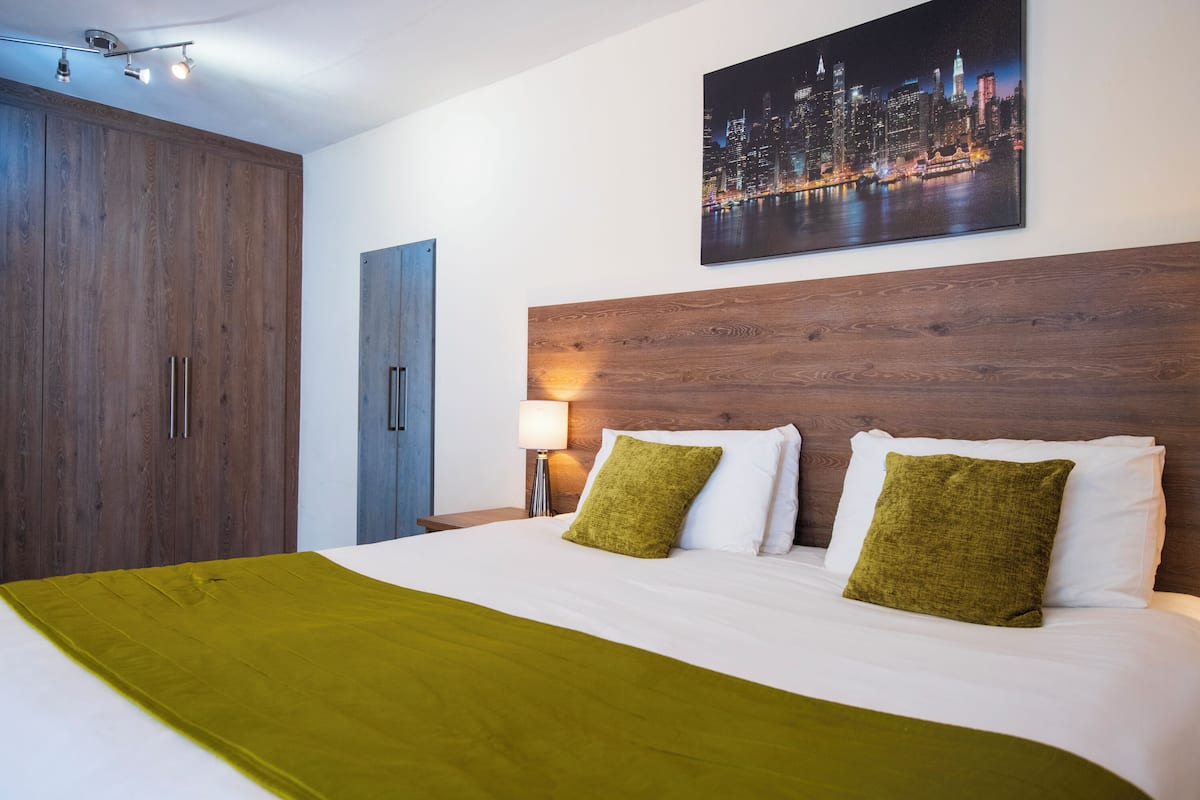 A hotel room with a large bed, a wooden headboard, a night cityscape painting, and a wardrobe.