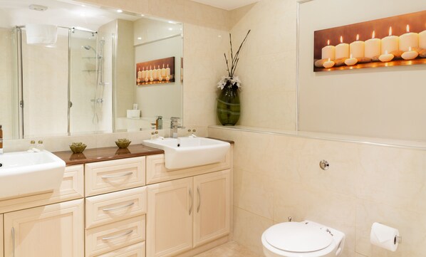 A modern bathroom with two sinks, a glass shower enclosure, a large mirror, and a vase with branches. - The Limes Country Lodge Hotel (Solihull)