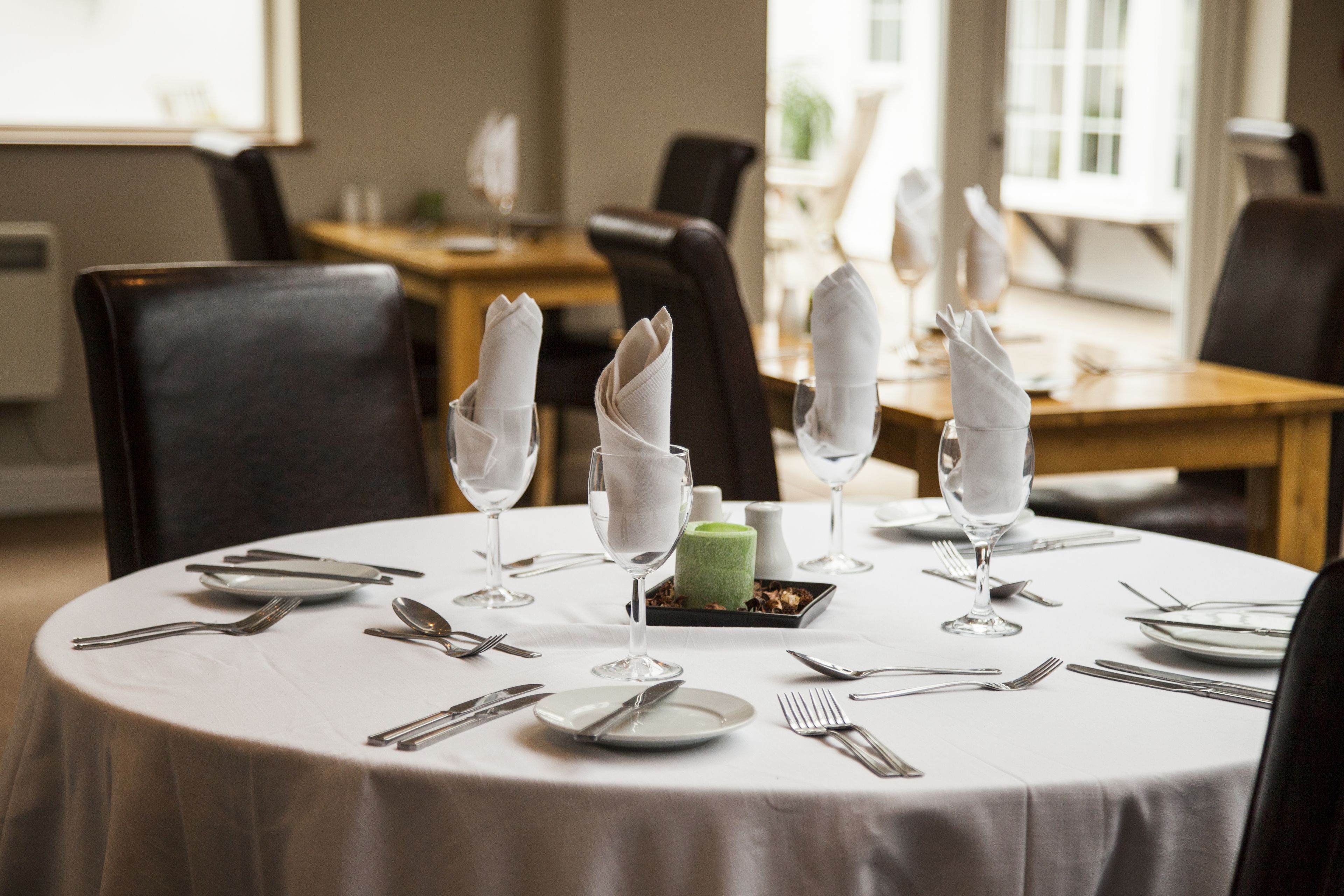 A round dining table set for a meal with white tablecloth, plates, cutlery, and folded napkins.