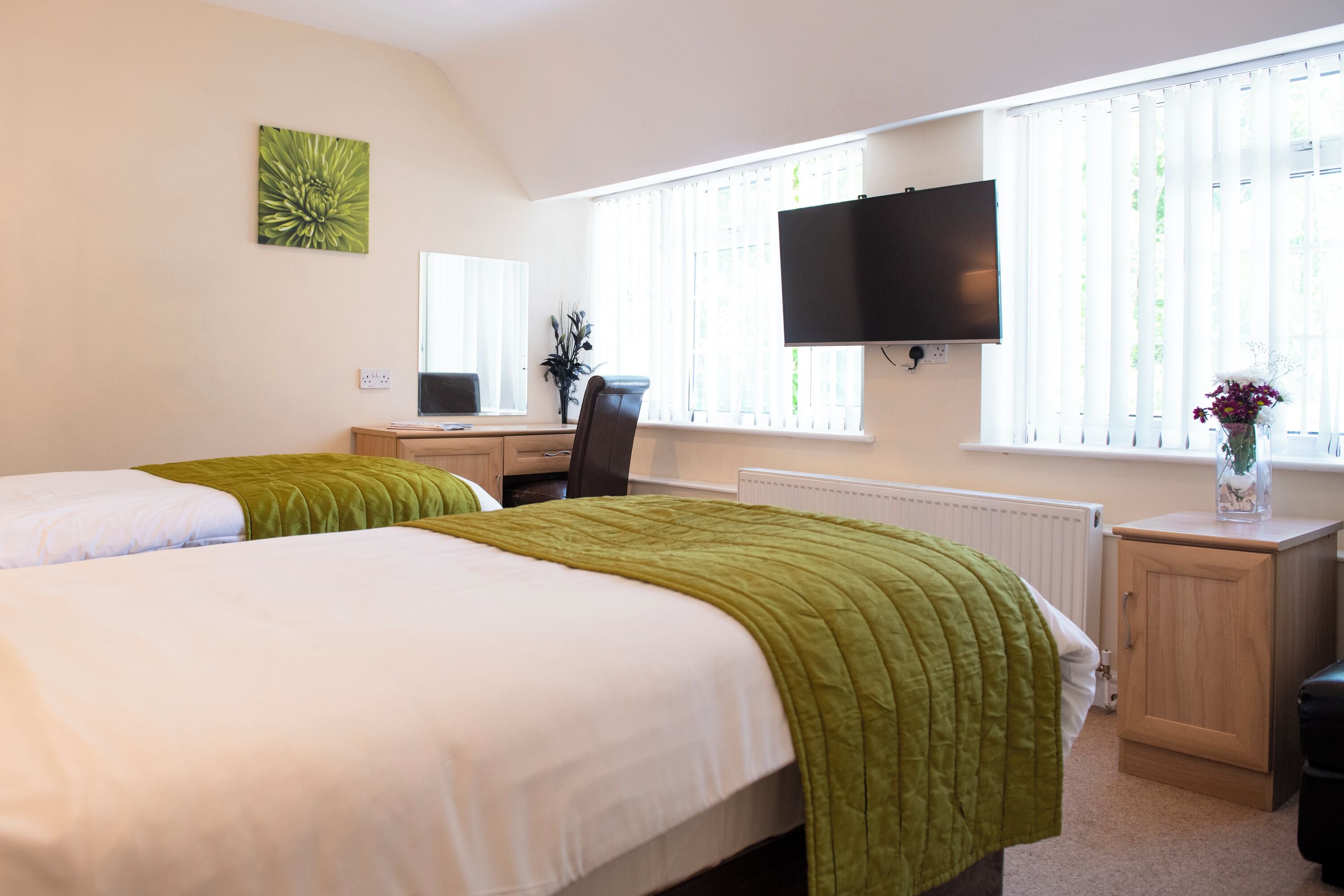 Een hotelkamer met twee bedden, een bureau met een computer, een televisie en een raam met jaloezieën.