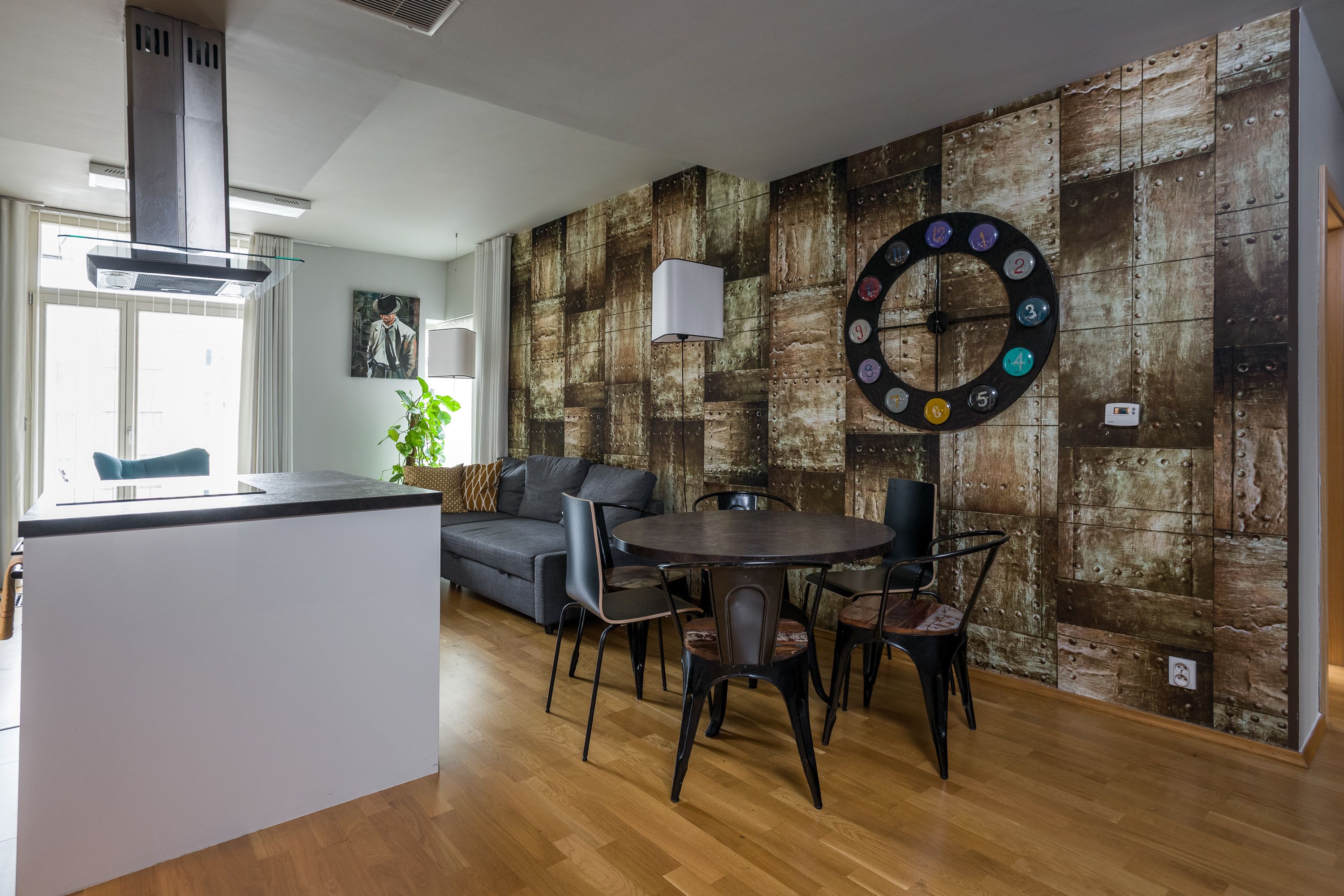 Una cocina moderna con una isla central, un comedor con una mesa redonda y sillas, y una pared con un reloj decorativo.