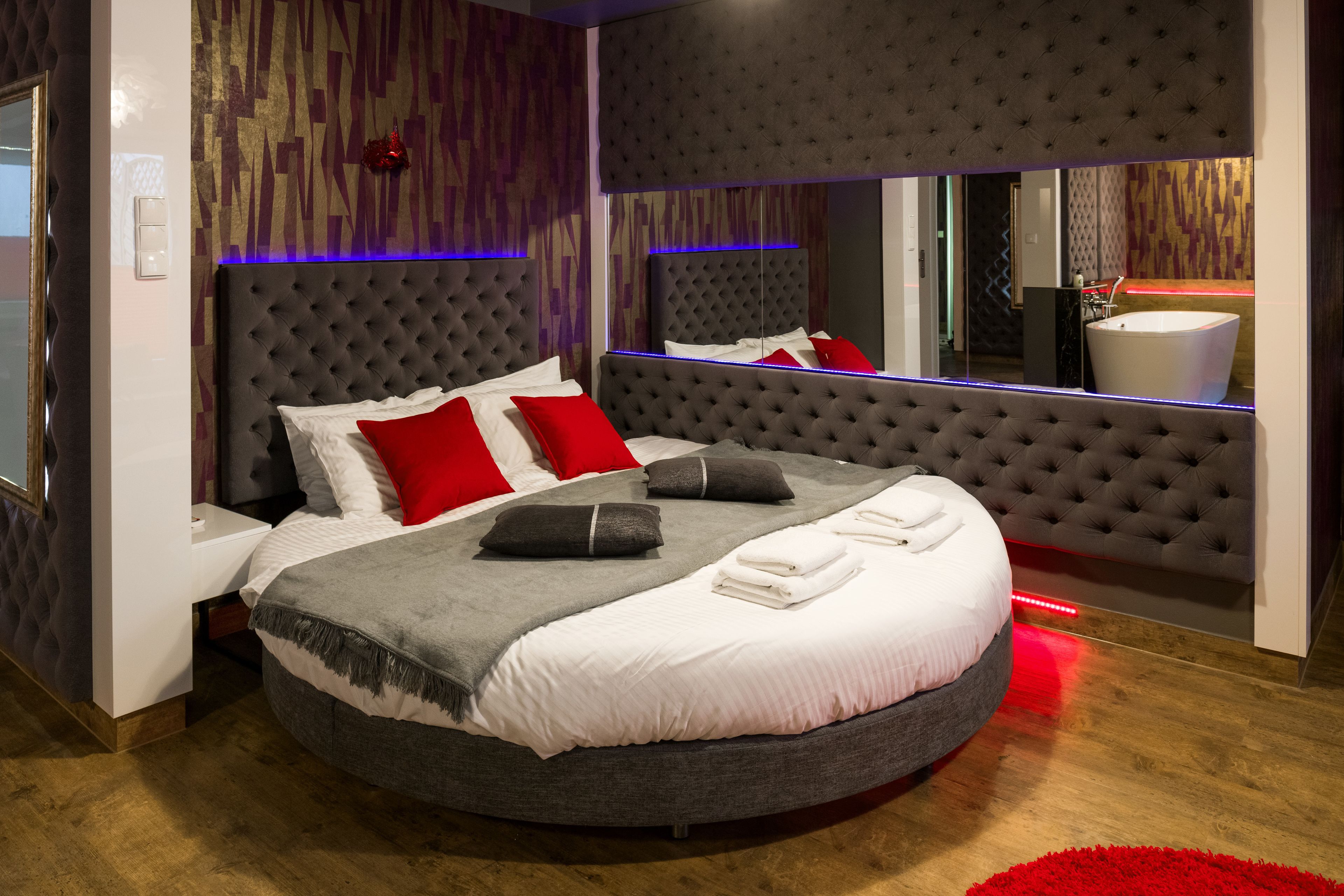 Ein rundes Bett mit einer gepolsterten Kopfteil, roten und weißen Kissen und einem Spiegel darüber.
