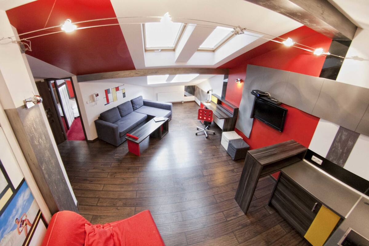 Ein moderner Wohnraum mit Schlafgalerie, einer Couch, einem Esstisch und einer Küchenzeile inklusive Fernseher.