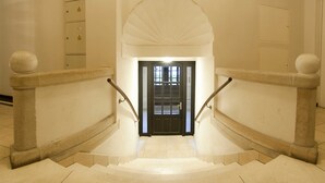 A grand staircase with a black door at the top, flanked by stone balustrades and a large arched ceiling.