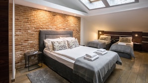 A bedroom with a brick wall, a skylight, a large bed, two bedside tables, and a smaller bed.