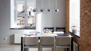 A dining area with a table, chairs, a window with a view of buildings, and hanging pendant lights.