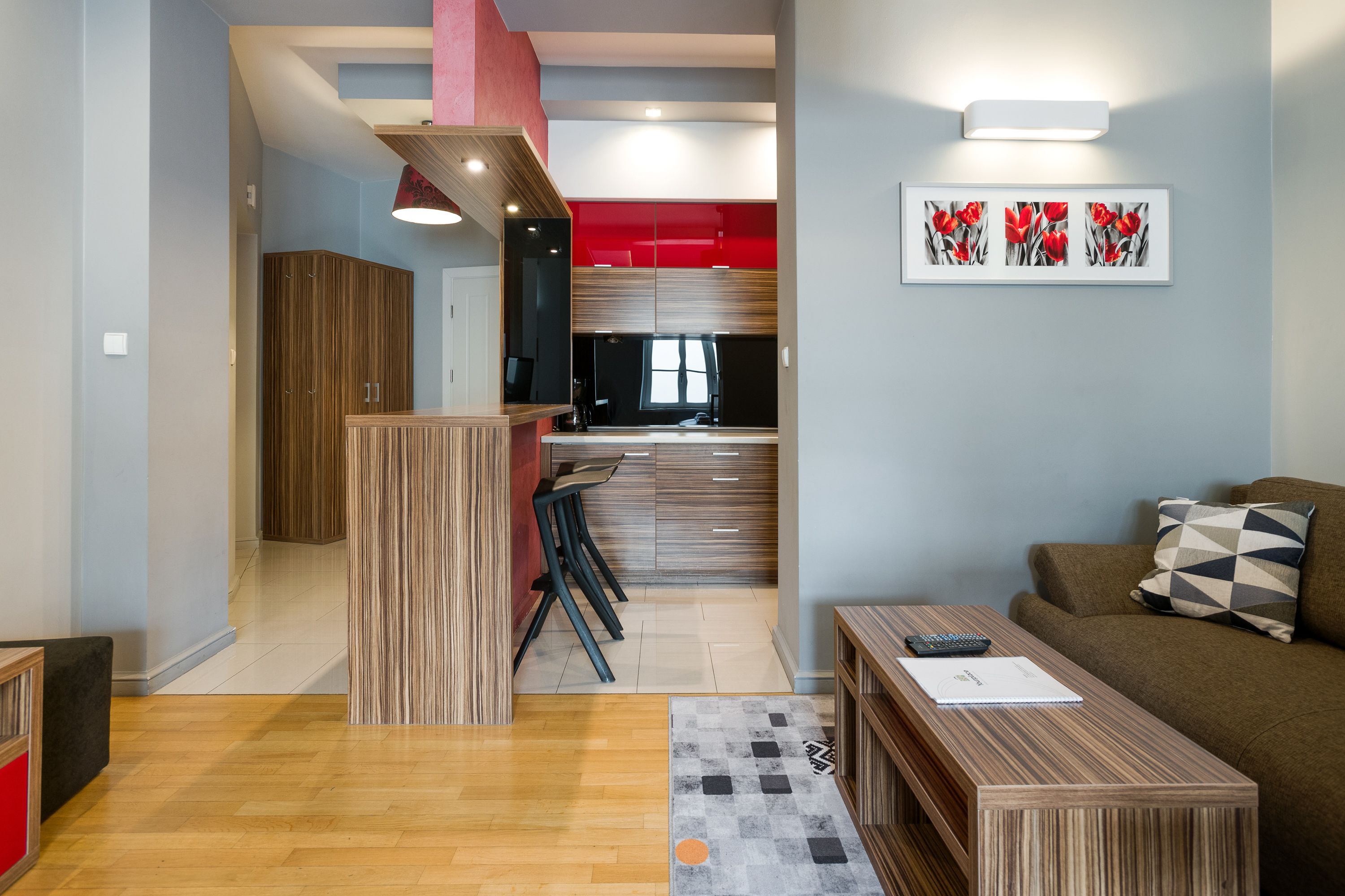 Una sala de estar moderna con una mesa de centro de madera, un sofá con cojines estampados y una zona de cocina con armarios rojos y una mesa de comedor.