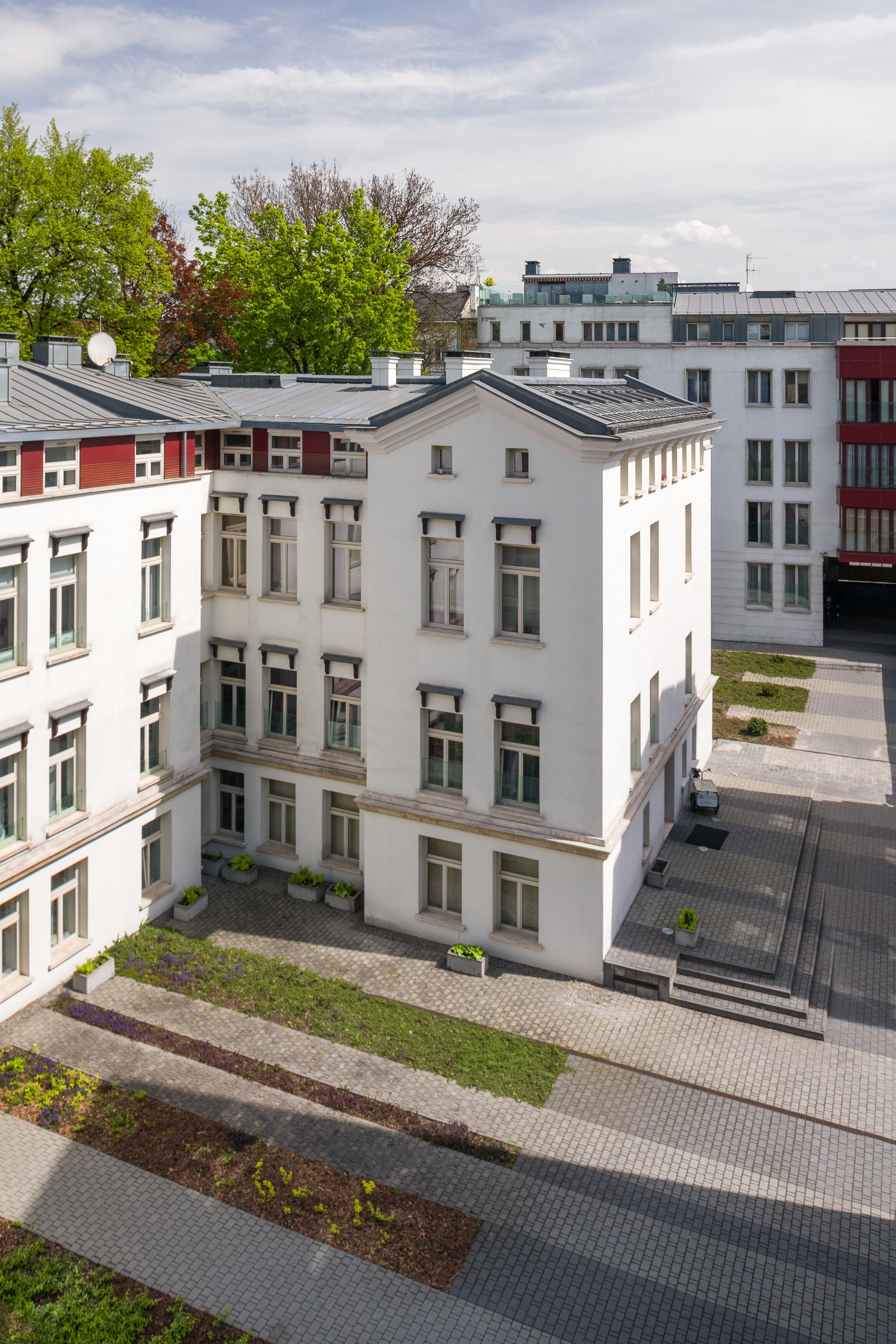 A multi-story building with a symmetrical facade, large windows, and a central courtyard with steps leading to the entrance.
