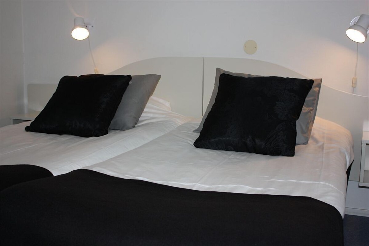 A double bed with white linens and black pillows, two bedside lamps, and a white headboard.
