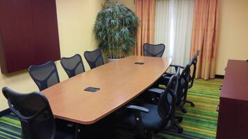 Una sala de conferencias con una larga mesa de madera, seis sillas de oficina negras, una planta en maceta y un armario rojo.