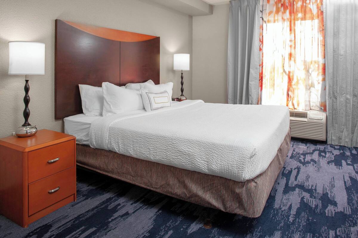 A hotel room with a large bed, two bedside tables, and a window with curtains.