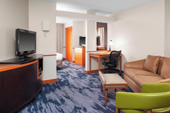 A hotel room with a desk, a television, a sofa, and a chair.
