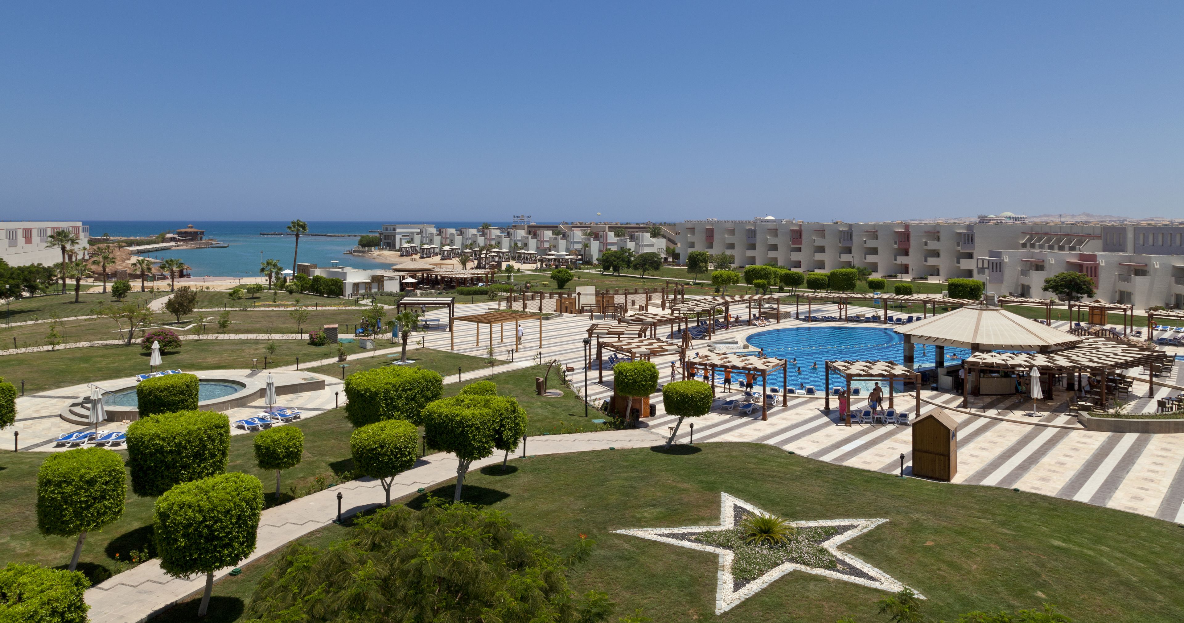 A resort with a central pool, multiple guest rooms, and a beach view.