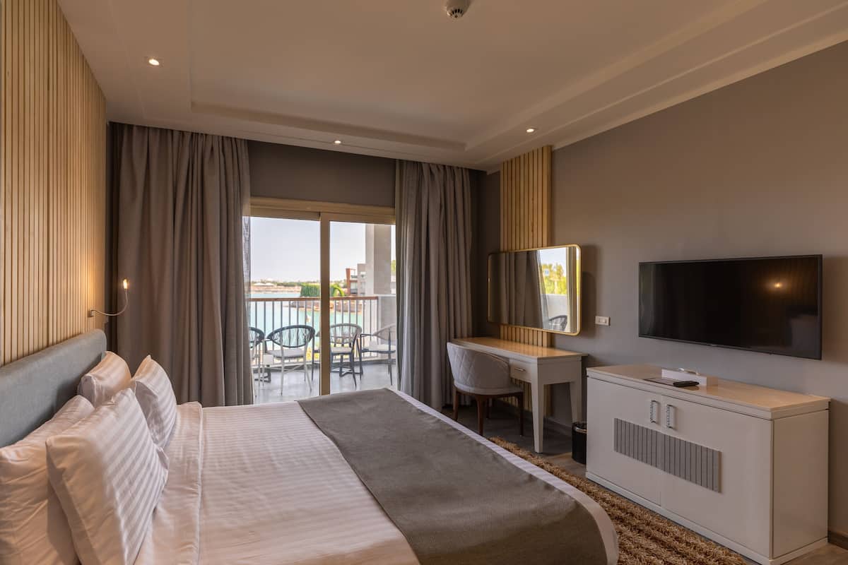 Habitación de hotel moderna con una cama grande, un escritorio, un televisor y un balcón con mobiliario exterior.