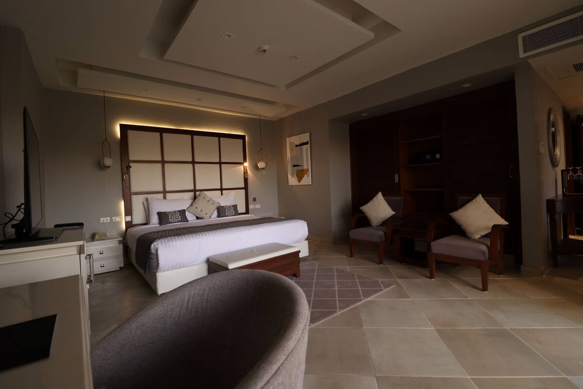 Habitación de hotel moderna con una cama grande, un escritorio, una silla y una zona de estar con sofá y sillones.