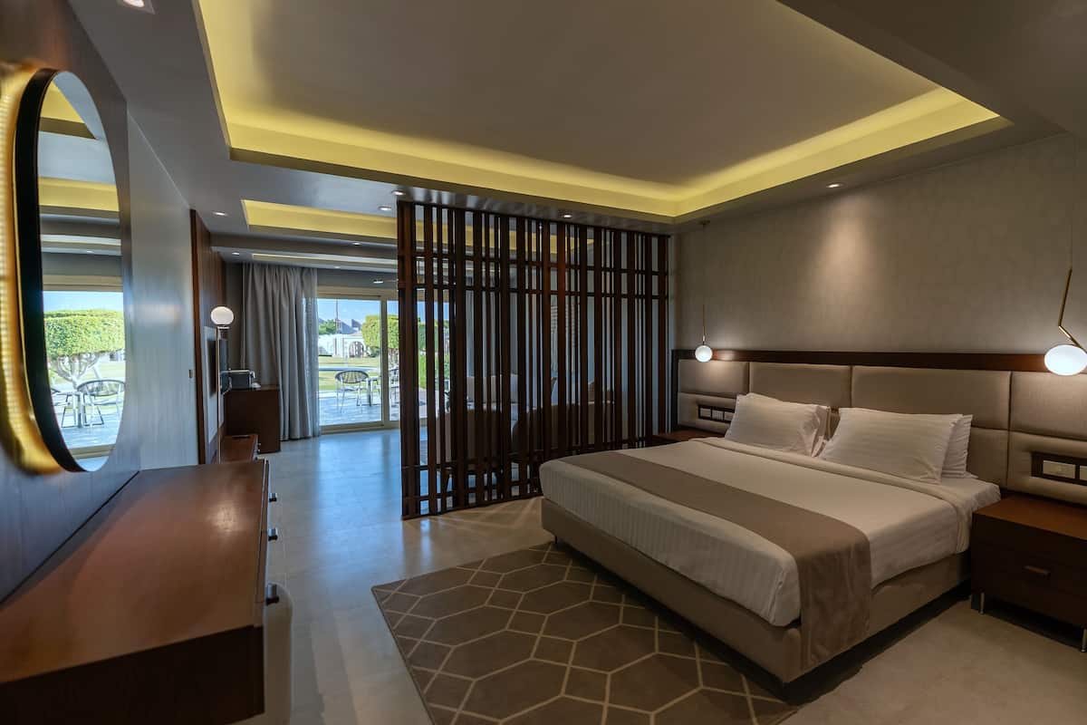 Un dormitorio moderno con una cama grande, mesitas de noche, un aparador y vistas a un espacio exterior a través de una puerta corredera.