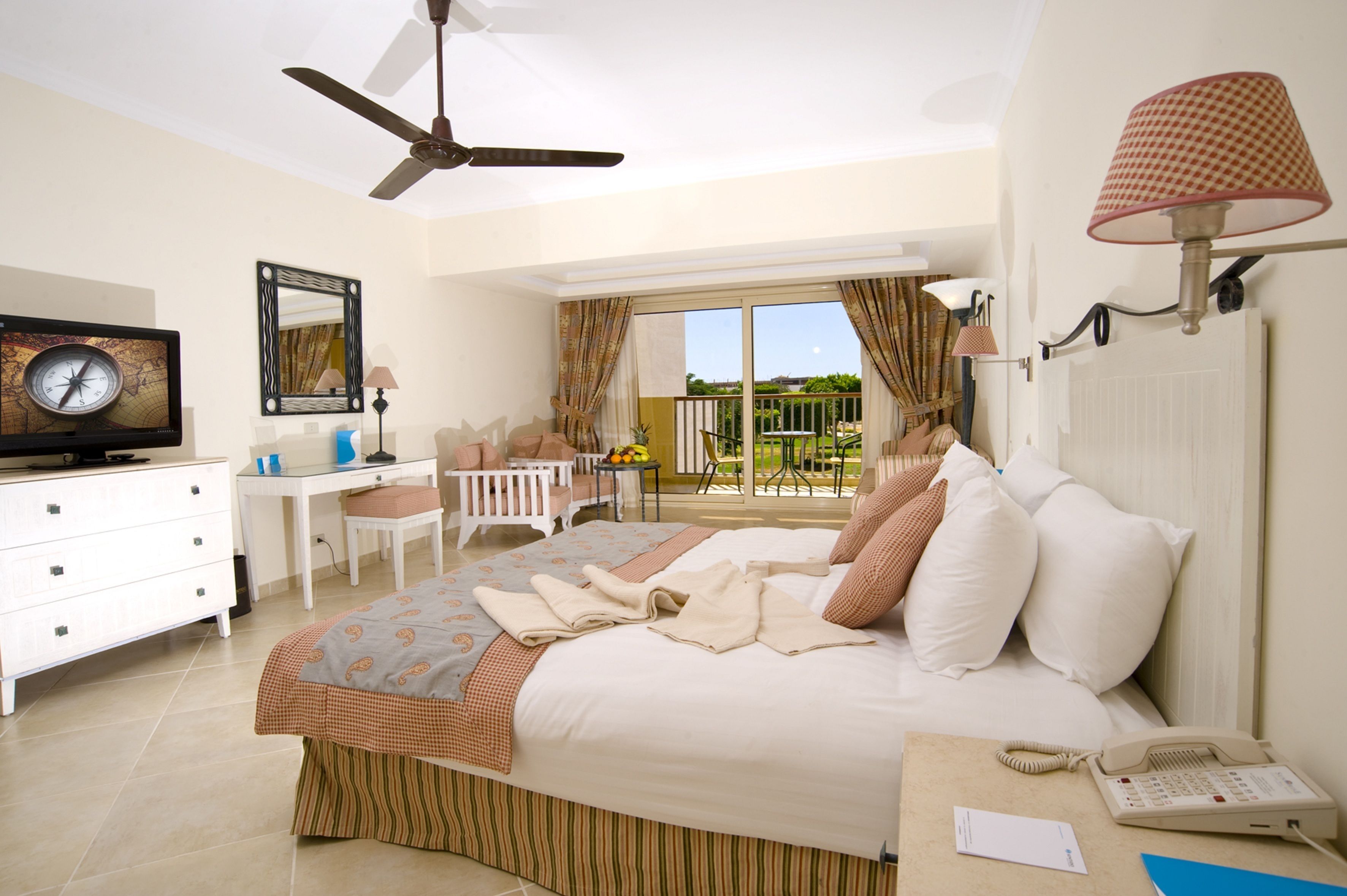 A hotel room with a bed, a desk, a chair, a TV, a phone, and a balcony with a view.