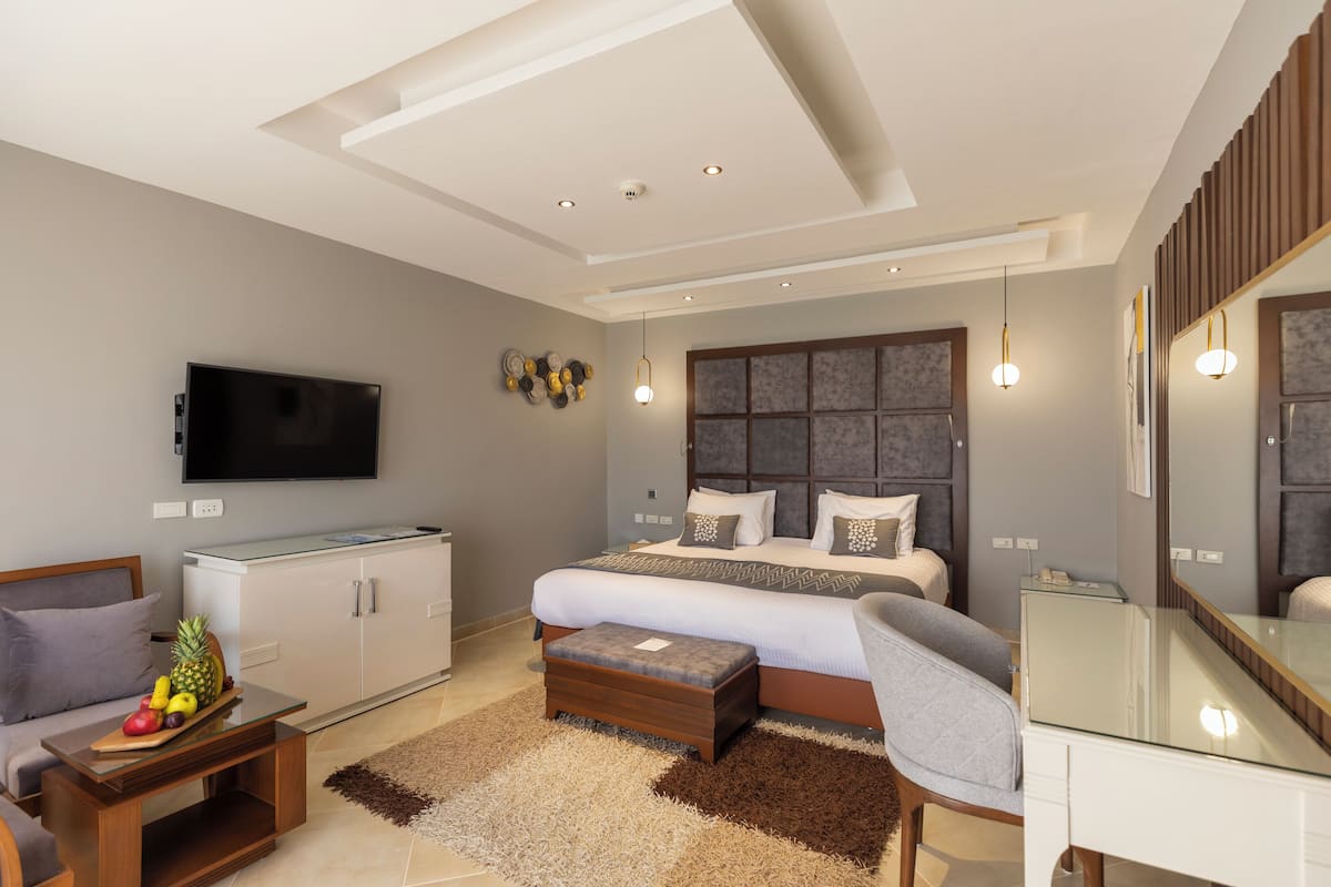 Un dormitorio moderno con una cama grande, un televisor montado en la pared, un escritorio y una zona de estar con una mesa de centro.