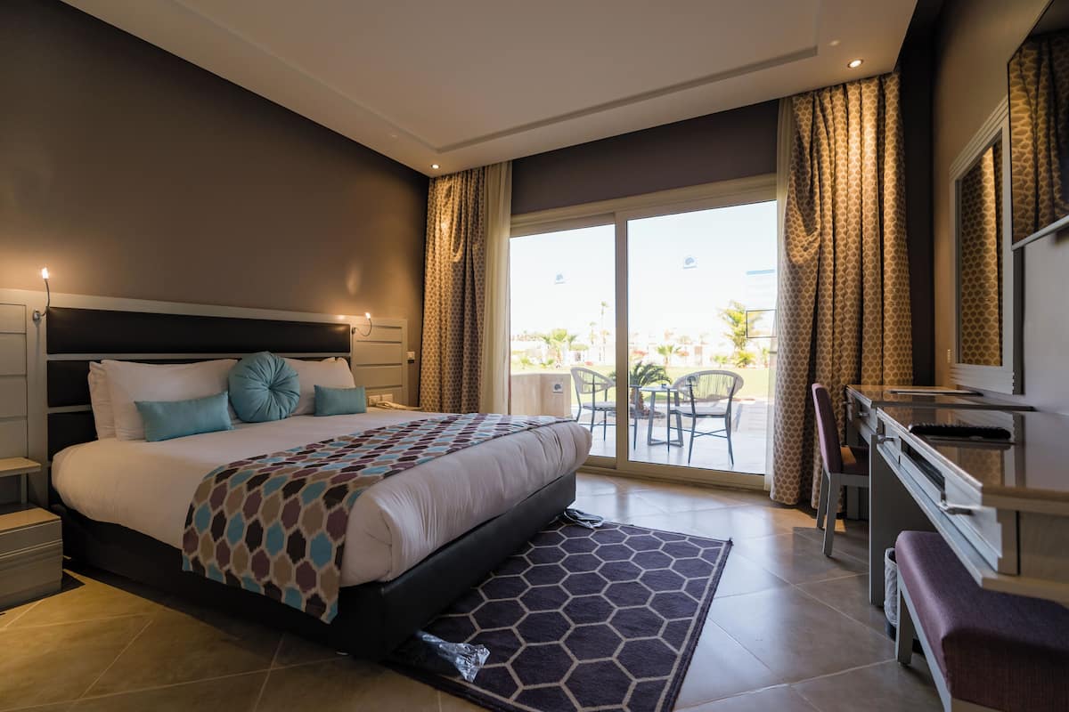 Una habitación de hotel moderna con una cama grande, un escritorio y un balcón con sillas.