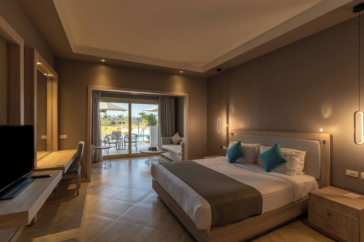 Habitación de hotel moderna con una cama grande, un escritorio y una televisión. Cuenta con un balcón y mobiliario exterior.