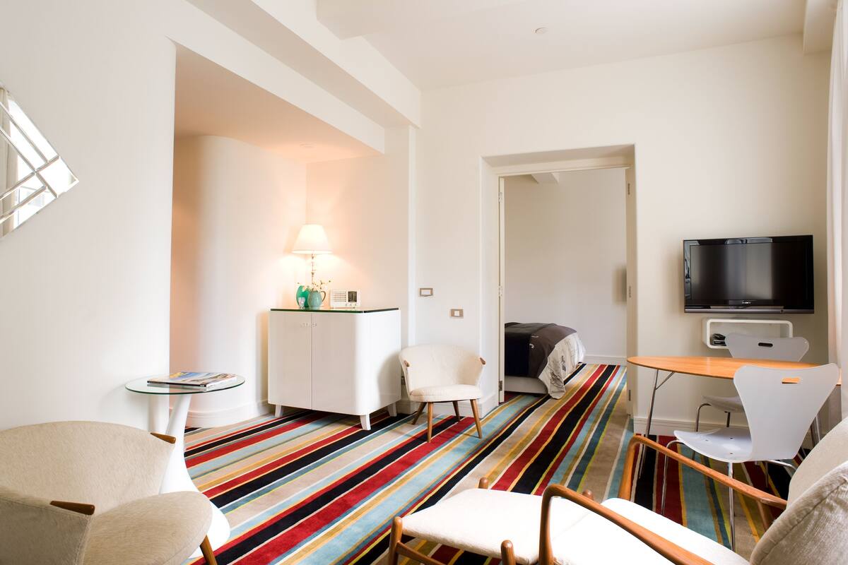 A modern hotel room with a striped carpet, a television, a desk, and a chair.