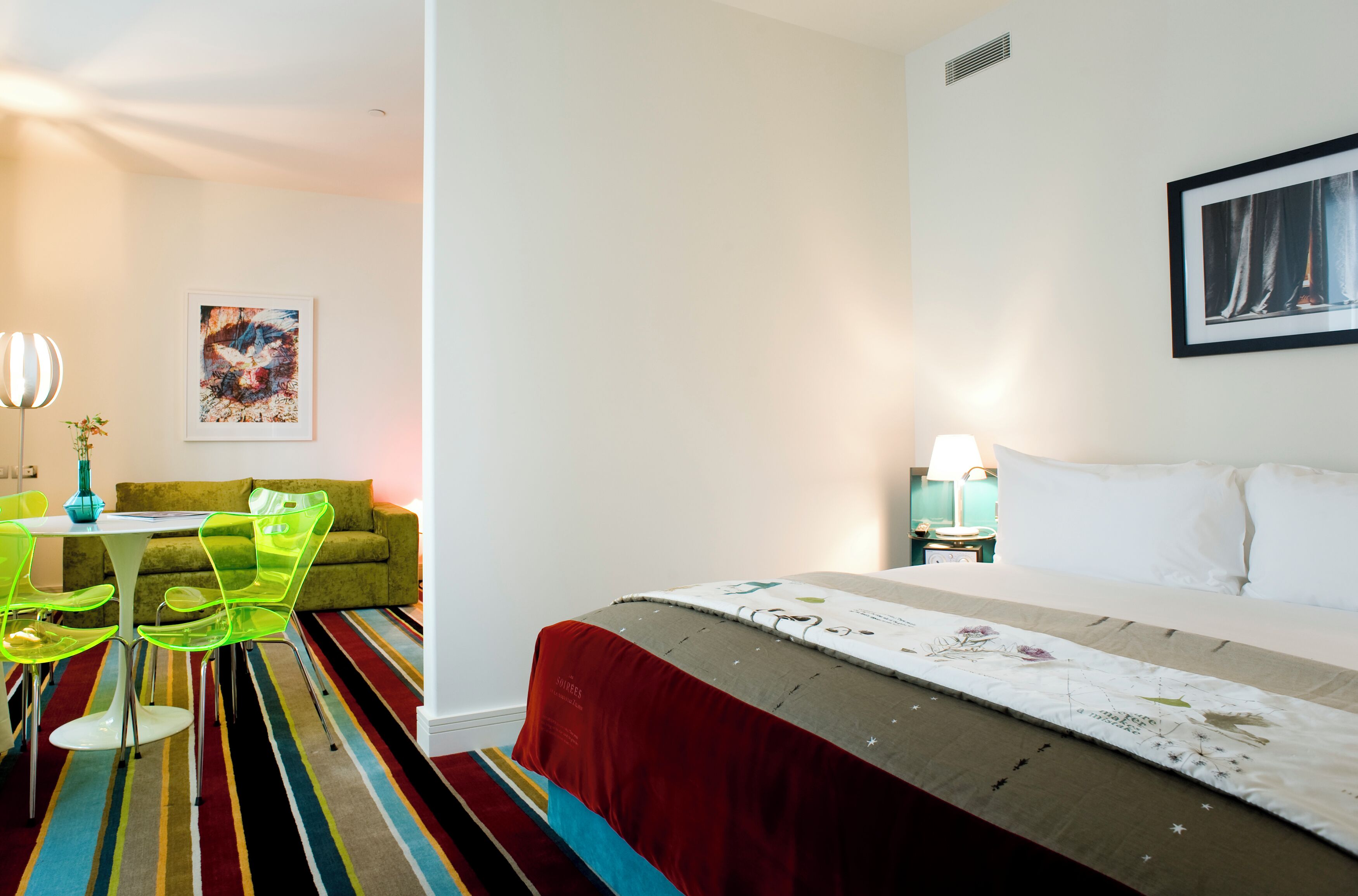 Una habitación de hotel con cama, una zona de comedor con sillas, una mesa y un colorido tapete a rayas.