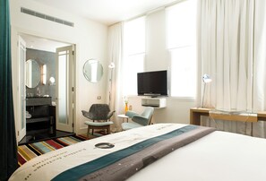 A hotel room with a bed, a TV, a desk, a chair, a mirror, and a bathroom visible through an open door. - Hotel DeBrett (Auckland)