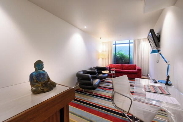 Una habitación moderna con un escritorio de madera, un sofá rojo, un sillón de cuero negro y una mesa de vidrio.