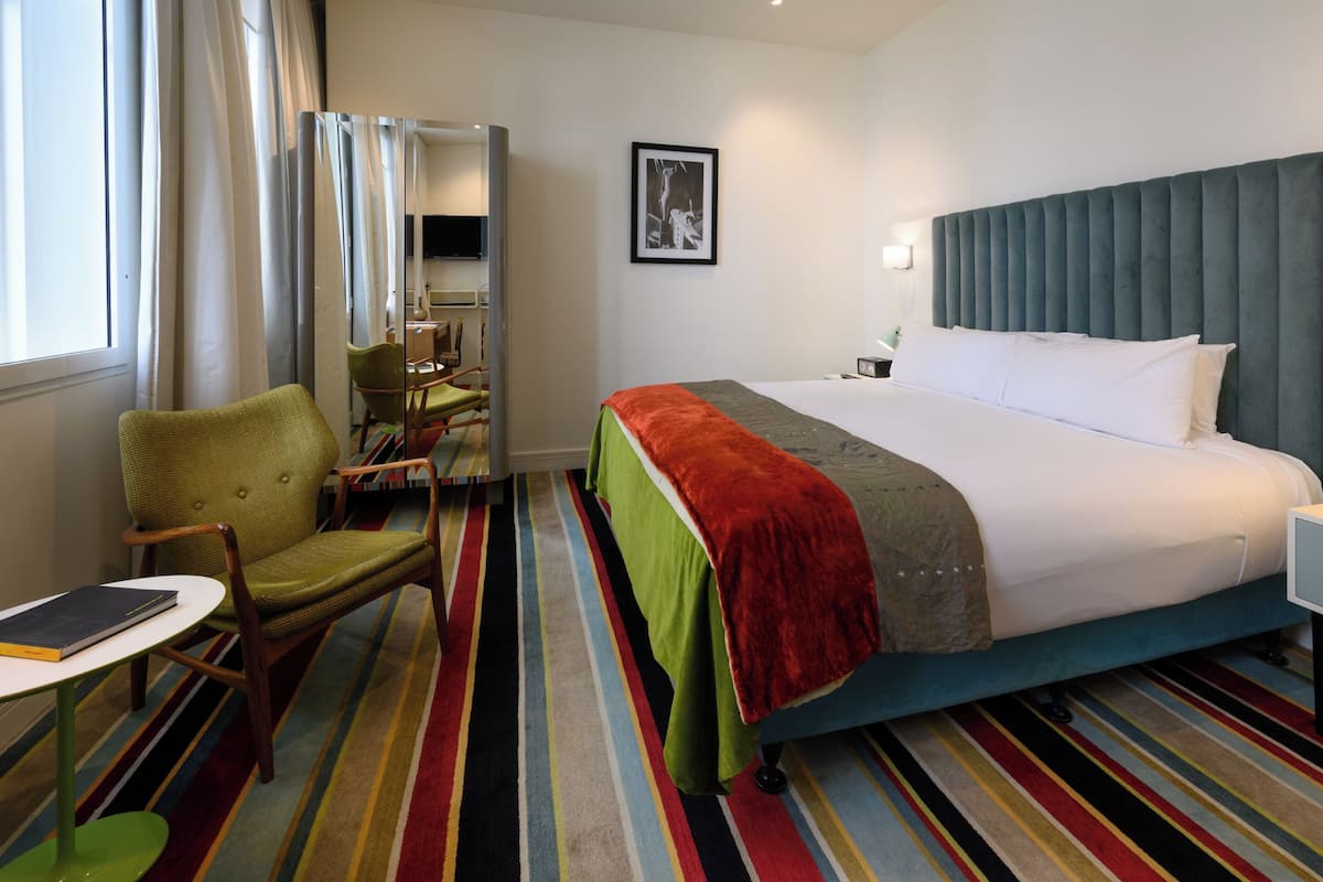 A hotel room with a bed, a chair, a small table, and a striped carpet.