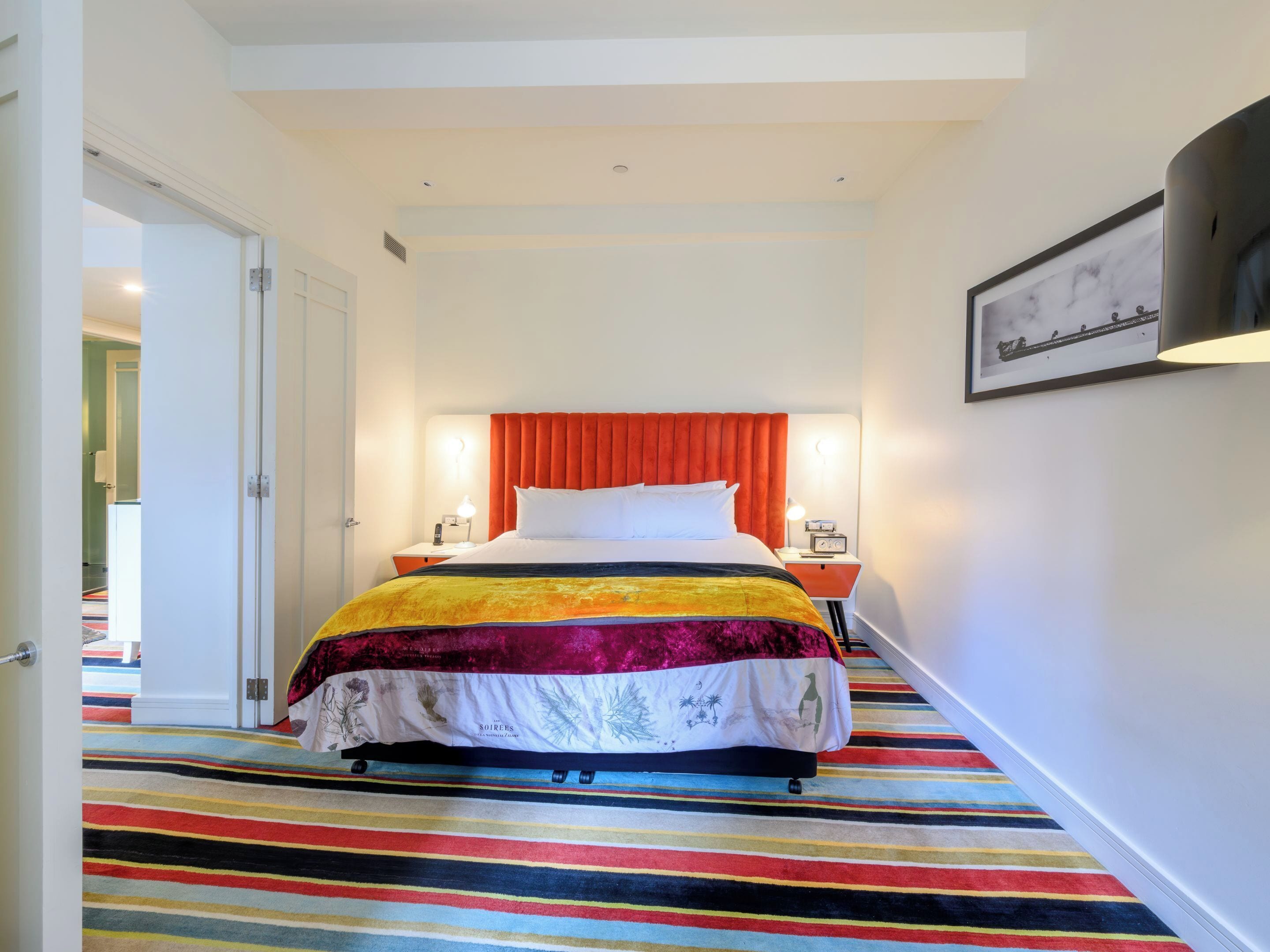 A hotel room with a bed, bedside lamps, a framed picture on the wall, and a striped carpet.