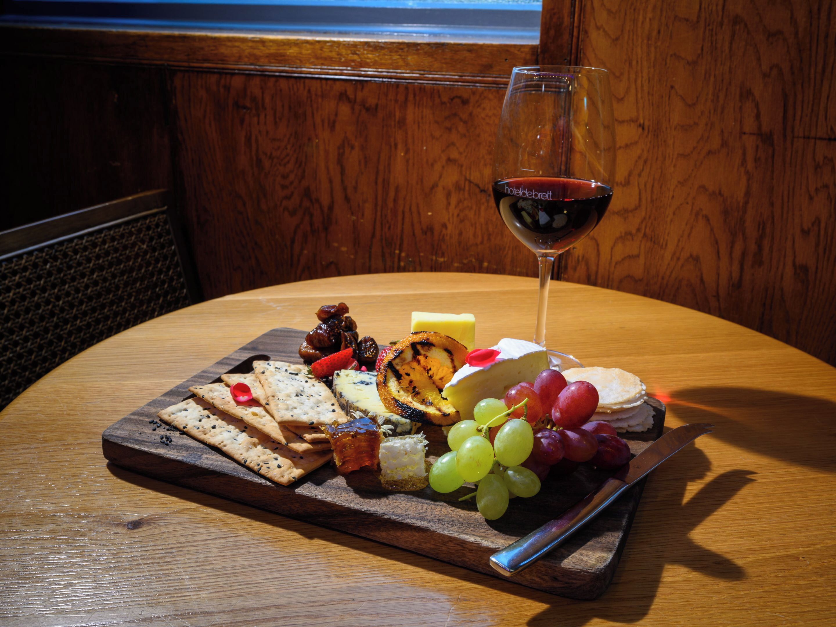 A wooden table with a charcuterie board featuring cheese, grapes, crackers, and a glass of red wine.