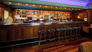 A bar with wooden shelves stocked with bottles, a cash register, and bar stools.