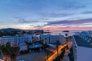A coastal hotel with multiple buildings, a swimming pool, and a view of the sea at sunset. - Hotel Caribe Ibiza (Santa Eulalia del Rio)