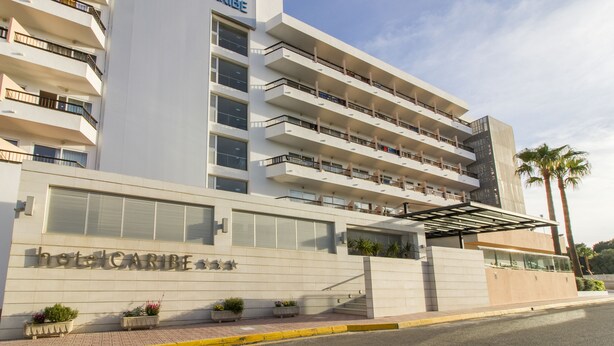 A multi-story hotel with balconies, a covered entrance, and a palm tree in the foreground.