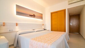 A hotel room with a bed, a wall-mounted artwork, a wooden door, and an air conditioning unit.