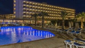 A hotel with a swimming pool, sun loungers, and palm trees.