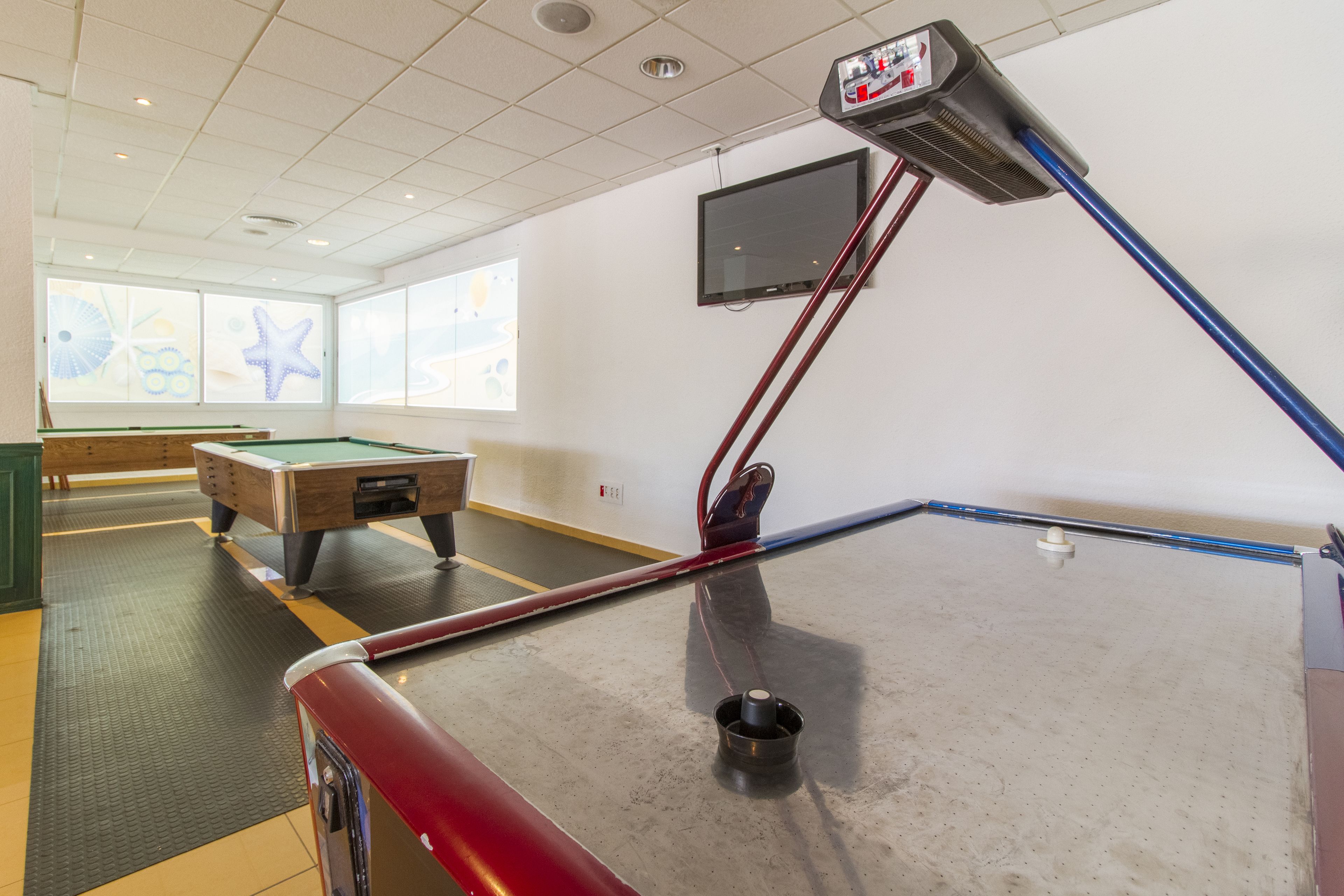 A billiards table with a mounted cue stick, a pool table, and a television mounted on the wall.