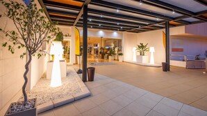 Een moderne hotelentree met een overdekt buitengebied, plantenpotten en een goed verlichte ingang.