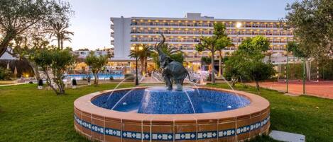 A courtyard with a fountain, a statue, and a hotel building in the background.