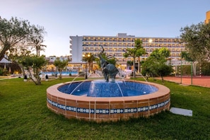 A courtyard with a fountain, a statue, and a hotel building in the background. - Hotel Caribe Ibiza (Santa Eulalia del Rio)