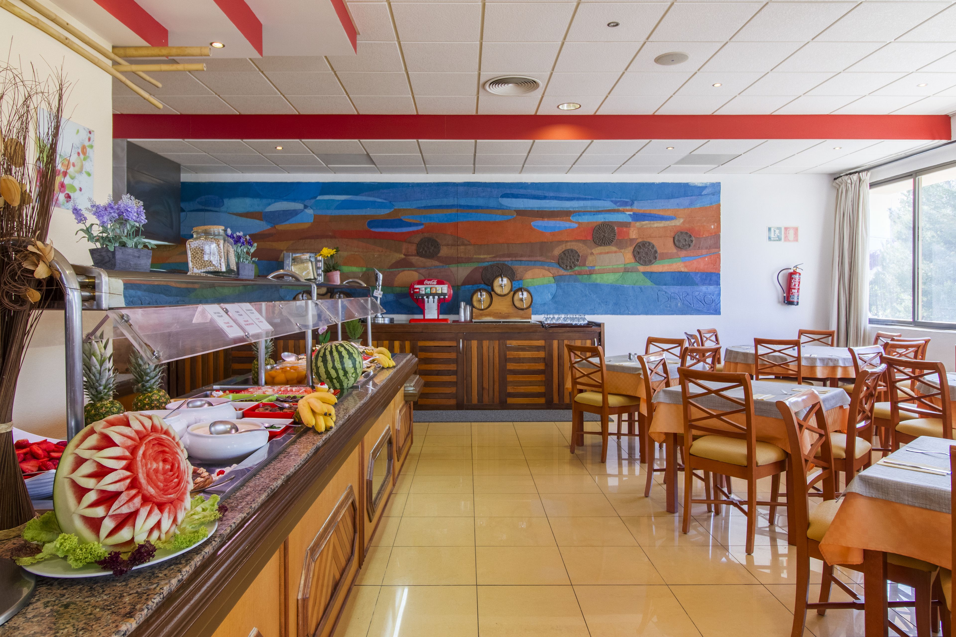 A restaurant with a buffet, wooden chairs, and a colorful mural on the wall.