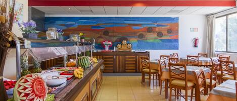 A restaurant with a buffet, wooden chairs, and a colorful mural on the wall.