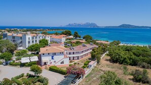 A coastal hotel with multiple buildings, a beach, and a mountain in the background. - Hotel Mare Blue (Olbia)