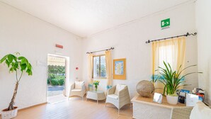 A hotel lobby with a reception desk, two wicker chairs, a potted plant, and a large window with curtains. - Hotel Mare Blue (Olbia)