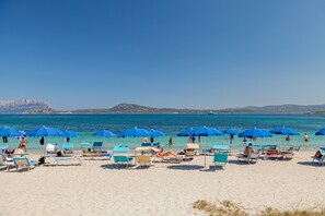 Una playa con filas de sillas de playa y sombrillas azules, un cielo azul despejado y mar en calma.