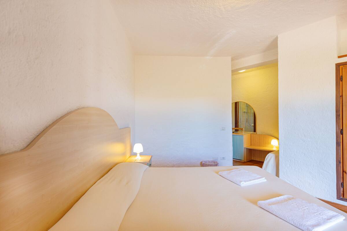 Ein Hotelzimmer mit einem großen Bett, Nachttischlampen, einer Holztür und einem Spiegel.