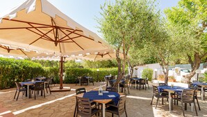 An outdoor patio with stone flooring, tables with blue tablecloths, and brown chairs. - Hotel Mare Blue (Olbia)