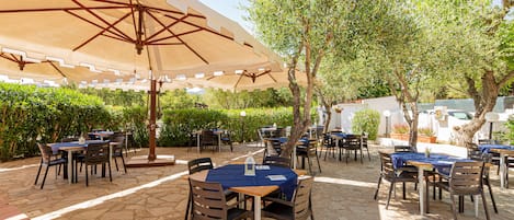 An outdoor patio with stone flooring, tables with blue tablecloths, and brown chairs.