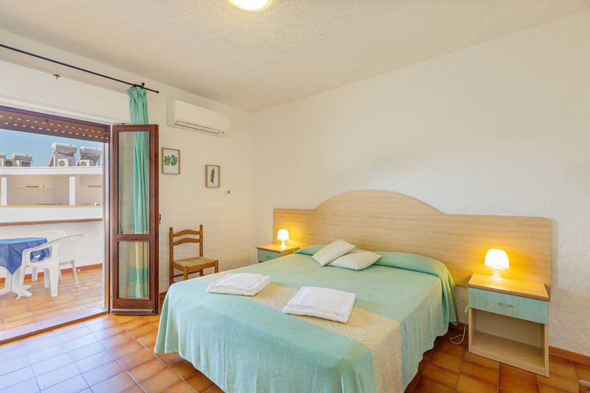 Ein Schlafzimmer mit einem Bett, zwei Nachttischen mit Lampen, einem Sessel, einem Tisch und einem Balkon mit Blick.